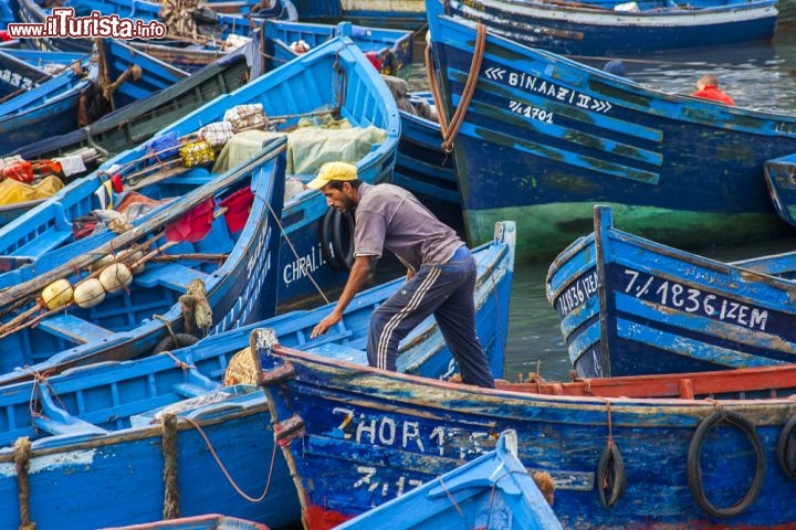 Immagine Barche colorate e pescatore a Essaouira, Marocco - Le imbarcazioni dei pescatori di Essaouira sono tutte ormeggiate in ordine nel grazioso porto della città. Con le loro mille tonalità del blu e dell'azzurro sono una delle tante attrazioni da non perdere durante una visita in Marocco © NOWAK LUKASZ / Shutterstock.com