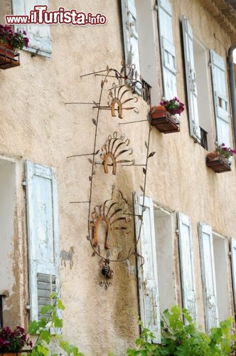 Immagine A decorare le facciate di edifici storici e dimore di questo villaggio non ci sono solo vegetazione lussureggiante e fiorita che profuma di erbe e essenze locali ma anche caratteristiche opere d’arte realizzate dagli artigiani