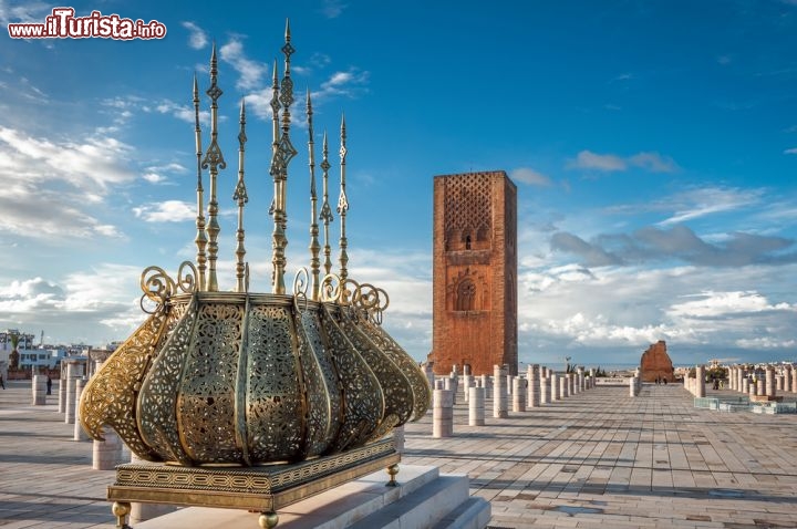 Immagine Rabat, la Torre Hassan: particolare di una decorazione dorata con l'emblema del Marocco, e sullo sfondo la Torre Hassan, simbolo della capitale Rabat, una delle storiche Città Imperiali marocchine - © foto360 / Shutterstock.com