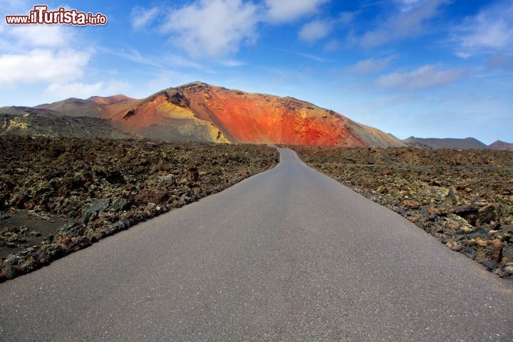 Immagine Strada dentro al Parco Nazionale di Timanfaya, a Lanzarote. Si tratta di uno dei parchi più affascinanti delle Canarie, caratterizzato da paesaggi vulcanici dall'aspetto lunare. Anche se le ultimi eruzioni in questa zona sud-occidentale di Lanzarote risalgono a circa 300 anni fa, il vulcano è ancora considerato come attivo, e ne sono testimonianza le elevate temperature del sottosuolo, che ragiungono vari di 600 °C a poche decine di metri di profondità. Il parco copre una superficie di circa 51 chilometri quadrati, ed l'elezione di Lanzarote a riserva della Biosfera dell'UNESCo è dovuta in massima parte alla sua presenza - © holbox / Shutterstock.com