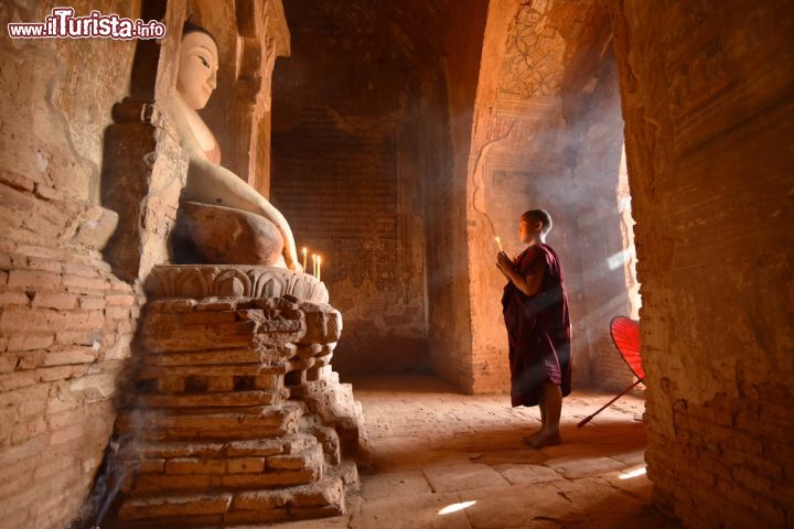 Immagine In preghiera al tempio buddhista di Bagan, Myanmar. In piedi dinnanzi alla statua del Buddha, questo giovane monaco prega rischiarato solo dalla luce di una candela - © jiraphoto / Shutterstock.com