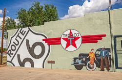 Fotografia di un dipinto sulla facciata di un edificio a Tucumcari, New Mexico, Stati Uniti. Una vecchia Chrysler, il logo Texaco, il simbolo della celebre Route 66, una donna e un cowboy - Sue ...