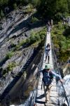 Giovani escursionisti attraversano un ponte sospeso sul torrente a Saint-Gervais-les-Bains, Francia. Siamo nell'area del ghiacciaio di Bionnassey - © Senderistas / Shutterstock.com