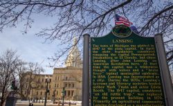 Insegna storica di fondazione della città di Lansing, Michigan (Stati Uniti d'America). Sullo sfondo il Campidoglio e la bandiera americana - © ehrlif / Shutterstock.com