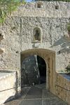 Uno scorcio della città castello di Saint-Paul-de-Vence, Francia. La strada acciottolata attraversa l'arco di uscita dalle mura in cui si trova una statua di San Paolo.

