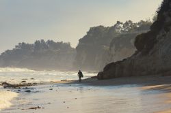Un surfista solitario cammina sulla spiaggia di Malibu, California.
