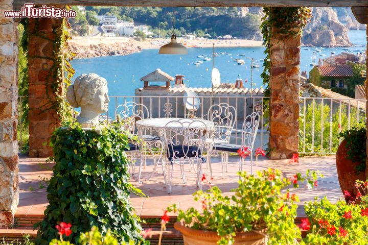 Immagine Un angolo di Tossa de Mar tra piante fiorite e mare splendente, in pieno stile mediterraneo - è un paesaggio tipico mediterraneo quello che accoglie i visitatori a Tossa de Mar, gioiello della Costa Brava. Questa splendida località, immersa tra scogliere di granito rosa, natura da macchia mediterranea e uno splendido mare pulito, con tanto di bandiera blu, è ricca di hotel e resort di lusso, meta ogni estate di migliaia e migliaia di turisti da tutta Europa. - © kavalenkau / Shutterstock.com