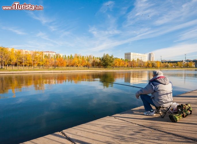 Immagine Veduta sul fiume Ishim, Astana - La moderna capitale del Kazakistan sorge sulle sponde del fiume Ishim con gli insediamenti abitativi più antichi situati nella zona nord e quelli più recenti su quella sud. Fiume, laghi e aree verdi della città si intersecano fra di loro in modo da favorire lo sviluppo della biodiversità. Le rive dell'Ishim sono state realizzate per preservare i paesaggi naturali circostanti così come per il vicino lago è stato studiato un apposito sistema per assorbire i flussi di piena conseguenti allo scioglimento delle nevi. In questa immagine, un pescatore seduto sulla sponda del fiume kazako © wassiliy-architect / Shutterstock.com