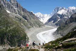 Veduta sul ghiacciaio Mer de Glace nel massiccio del Monte Bianco, Chamonix (Francia). In primo piano, un gruppo di escursionisti in cammino in una giornata estiva di sole.


