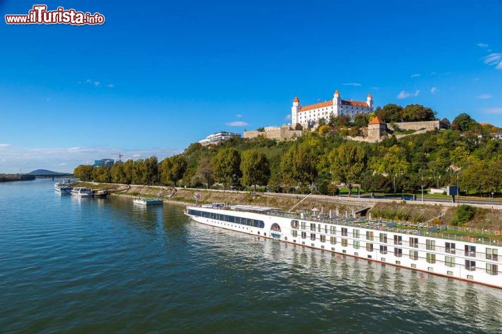 Immagine Il fiume Danubio con le imbarcazioni ormeggiate sulla banchina in primo piano e, sullo sfondo, la collina sulla quale svetta il castello di Bratislava - foto © S-F / Shutterstock.com