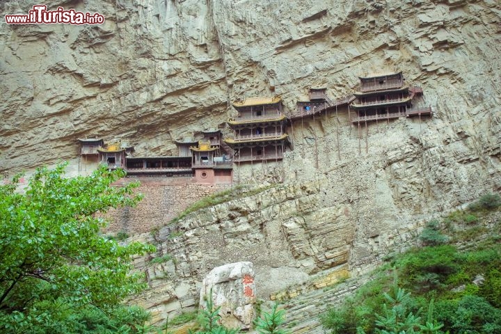Monastero Xuan Kong, in Cina - Il monastero cinese di Xuang Kong a Datong, che non a caso è soprannominato “il monastero sospeso”, sembra aggrappato in equilibrio precario su una parete rocciosa ai piedi del monte Heng, a strapiombo sul canyon del Jinlong, nella privincia di Shanxi. Apparentemente basterebbe una folata di vento a distruggere la leggiadra creazione, che invece resiste sulla roccia da oltre 1400 anni e oggi è una delle attrazioni turistiche più famose della zona. La posizione non fu scelta per motivi scenografici, ovviamente, ma perché garantiva protezione dalle inondazioni e perché la cima della montagna avrebbe bloccato pioggia e neve provenienti dall’alto; in più, una motivazione “acustica”: l’ampia parete verticale – che cattura i suoni e li fa scivolare via – assicura un silenzio praticamente assoluto, come vogliono i principi del taoismo. Taoismo ma anche buddismo e confucianesimo trovano un’armonica sintesi in questo antico monastero, che oltre a un luogo sacro rappresenta un’opera ingegneristica notevole, ammirata ogni anno da visitatori di tutto il mondo: tra gli ospiti c’è chi cerca un’ispirazione spirituale e chi invece ha la passione per l’architettura e vuole studiare questo miracolo sospeso. Parzialmente ricostruito durante la dinastia Ming (1368-1644) e Qing (1644-1911), il monastero di Xuan Kong custodisce più di ottanta sculture variopinte realizzate in pietra, terracotta, rame o ferro, e rappresenta un grande testimone della storia e della cultura cinesi.
Come arrivare? Il monastero di Xuan Kong sorge a 65 km circa da Datong, raggiungibile in treno o in autobus da Pechino: l’autobus impiega meno tempo (4 ore circa), ma il treno ha il vantaggio di viaggiare di notte e scaricarvi a Datong all’alba, quando lo scenario è ancor più affascinante - © Tepikina Nastya / Shutterstock.com