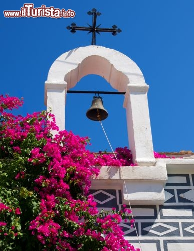 Immagine Nel villaggio di Pyrgi, sull'isola greca di Chios, i simboli cristiani della croce e della campana si stagliano contro un cielo azzurro intenso. Bellissimo il contrasto del bianco, del blu e della buganvillea fucsia - © Steliost / Shutterstock.com