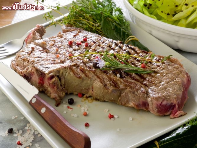 Immagine Bistecca alla Fiorentina. La bistecca con l'osso è uno dei piatti classici della cucina toscana e di Firenze, assieme ai piatti classici come la ribollita, i fagioli all'uccelletto, il baccalà, i cenci, il castagnaccio, il lampredotto e la trippa. La Fiorentina è uno dei pezzi forti dei ristoranti in centro a Firenze ed il taglio prevede un peso di almeno 1,2-1,5 kg, per pezzo. Tenetene conto quando l'ordinate! - © marco mayer / Shutterstock.com
