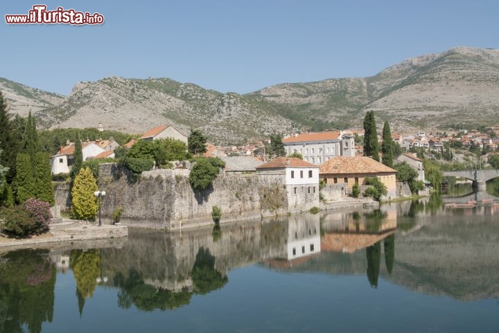 Immagine Scorcio panoramico sul borgo di Trebinje, Bosnia Erzegovina - Piazze alberate, centro storico e paesaggio bucolico sono i fiori all'occhiello di questo villaggio bosniaco che richiama ogni anno migliaia di turisti provenienti da tutto il mondo. Ancora oggi, nonostante le dimensioni piuttosto ridotte, a richiamare l'attenzione dei visitatori è ciò che rimane della cinta muraria di un tempo. Alcuni bastioni dell'imponente costruzione si affacciano sul lungofiume specchiandosi nelle sue acque limpide © photovlada / Shutterstock.com