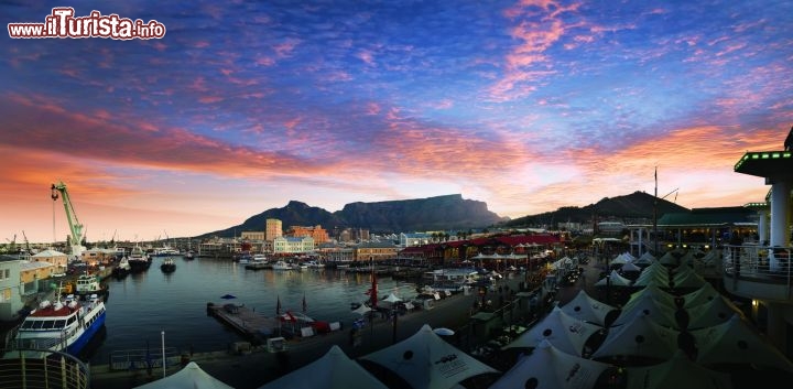 Immagine Cape Town al tramonto - Quando ci troviamo di fronte alla bacchetta magica che sa avere solo un tramonto, le reazioni di solito sono due. La prima è quella di cercare un posto per ammirarlo al meglio e la seconda è quella di prendere la macchina fotografica, già sapendo però che si sta per immortalare qualcosa di già visto. Quello che accade davanti al tramonto di Cape Town invece ha una marcia in più: ogni sole che va a riposare non è mai uguale a quello del giorno precedente a seconda della posizione in cui ci si trova. Grazie al gioco di luci sull'acqua del molo come si vede dall'immagine, qui le sfumature del cielo sono moltissime - Fonte South African Tourism