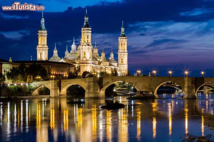 Immagine Il centro storico di Saragozza visto dal fiume Ebro e la Cattedrale illuminata. Di notte, con le luci delle strade e dei palazzi che si riflettono sull'acqua, la città araba e europea diventa ancora più magica - © Simone Simone / Shutterstock.com