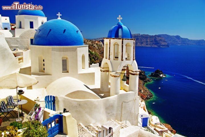 Immagine Le chiese di Santorini, con le paricolari cupole blu, sullo sfondo la caldera del Vulcano Neo Kameni: siamo nell'arcipelago delle Cicladi in Grecia - © leoks / Shutterstock.com