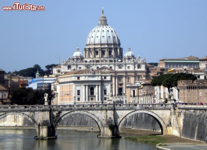 Immagine La Basilica di San Pietro (Roma) con la sua cupola vista dal ponte Sant'Angelo, sul fiume Tevere. La chiesa cattolica più grande del mondo si vede da molti punti panoramici della capitale, fulcro della cristianità, punto di riferimento per i fedeli e attrazione irresistibile per i turisti. Le dimensioni sono colossali: 218 m di lunghezza massima esterna per 115 m di larghezza della facciata.