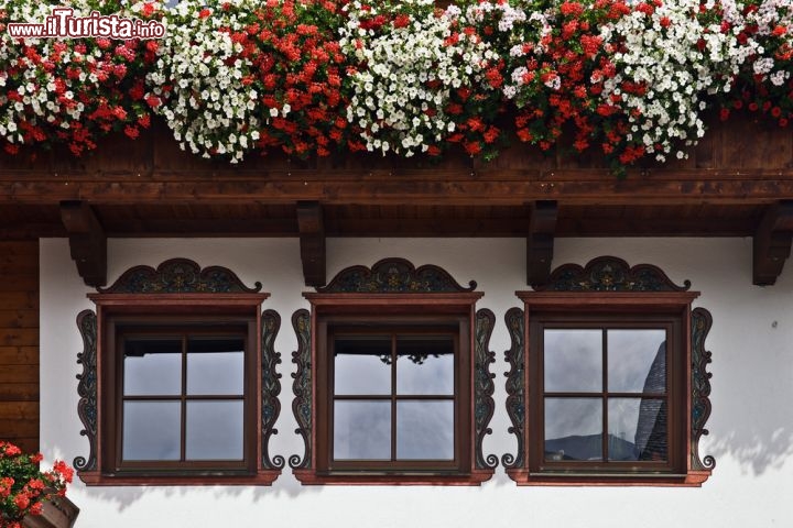 Immagine Un particolare di finestre e balcone fiorito in Alpbach, Tirolo (Austria) - Se c'è una specialità che questa città tedesca del Tirolo può vantare in modo magistrale, senza dubbio è il suo gusto estetico. Case di legno (il materiale più semplice dell'edilizia) arricchite dalle decorazioni in stile principesco (le linee dalla forma più lussuosa), con dei fiori così colorati, aperti e pieni da far dimenticare i primi due punti. Un trittico decisamente azzardato, tanto da aver regalato ad Alpbach dei davanzali che sembrano scoppiare dalla voglia di vivere e di farsi ammirare da tutti i suoi visitatori, cittadini stessi compresi - © Khirman Vladimir / Shutterstock.com