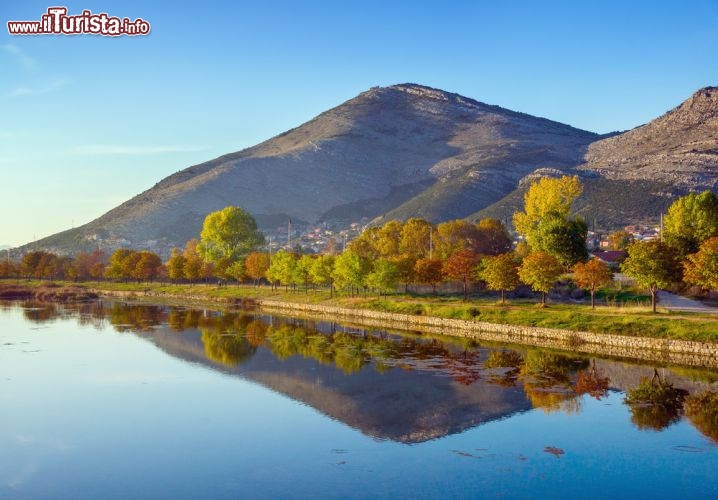 Immagine Fiume Trebisnjica, Bosnia Erzegovina - Foliage autunnale con tonalità dal giallo al rossastro per gli alberi e la vegetazione che si rispecchiano sul fiume Trebisnjica conosciuto anche come "fiume che affonda". Lungo i suoi 187 chilometri, questo corso d'acqua rappresenta una delle bellezze paesaggistiche da non perdere durante un tour nel centro amministrativo della regione Trebinje che fa parte della Repubblica di Bosnia Erzegovina © Olga Ilinich / Shutterstock.com