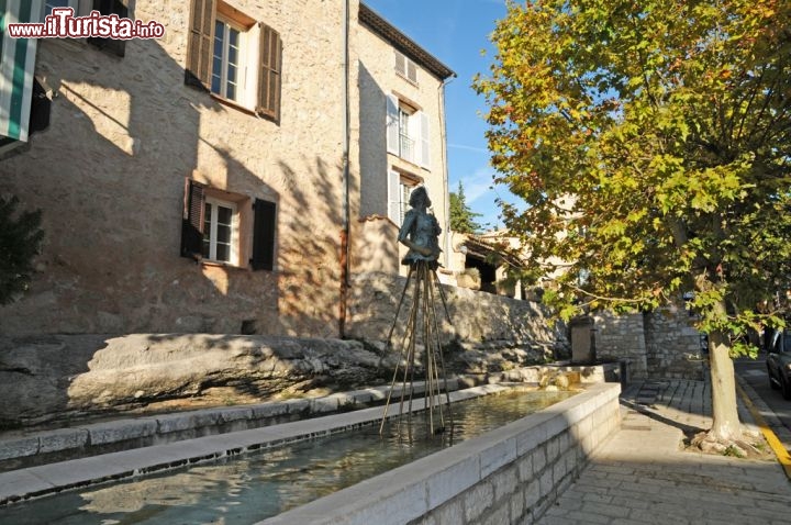 Immagine Fontana con statua, Tourrettes sur Loup - Sulla via principale del paese, quella che taglia a metà il villaggio e che conduce verso Grasse e Vence, si affaccia una grande vasca d'acqua a forma rettangolare impreziosita da un gruppo scultoreo composto da un busto che poggia su dei piedistalli. E' solo una delle tante costruzioni che abbelliscono il paese di Tourrettes sur Loup © Sonja Vietto Ramus