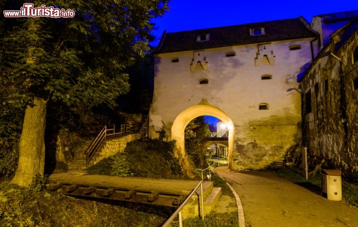 Immagine Scorcio notturno sulla città vecchia di Brasov, Romania - Furono i sassoni a scegliere questo territorio dell'attuale Romania per fondare una nuova colonia mercantile battezzata all'epoca Kronstadt. E furono sempre loro a costruire la maggior parte delle abitazioni che sorgono nel centro storico così come alcune chiese e la cinta muraria difensiva, tutt'ora ben conservata, che abbraccia la città. In quest'immagine scattata al calar del sole, la fortificazione dell'antica città di Brasov in tutto il suo fascino medievale © Christian Draghici / Shutterstock.com