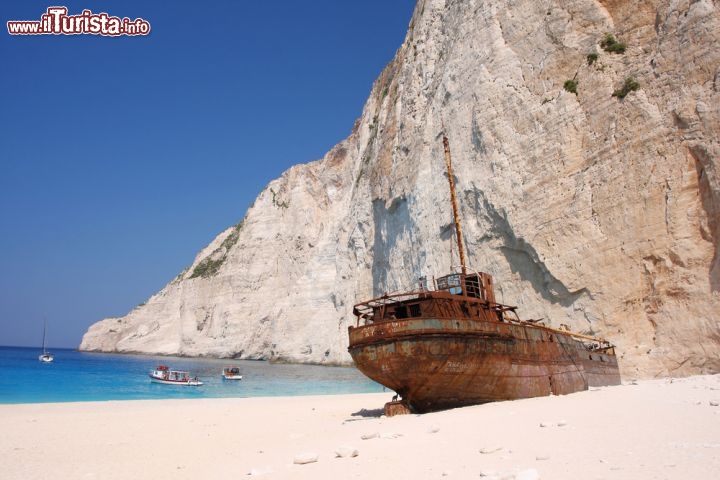 Immagine Il relitto della spiaggia di Navagio a Zante (Zacinto). Non tutti sanno che la nave Panagiotis era una imbarcazione che contrabbandava sigarette. Durante una fuga notturna, nel 1980, venne intercettata dalla guardia costiera, e si rifugiò in questa stretta baia, della costa ovest di Zante. La nave però si arenò su di una barra sommersa. Incredibilmente, la massa della nave da allora ha smorzato l'energia delle onde, consentendo la formazione di un arenile costituito da sabbie e piccoli ciottoli. La presenza poi di sorgenti sulfuree rende particolare il colore delle acque, creando un ambiente che non ha uguali nel mondo - © Samot / Shutterstock.com