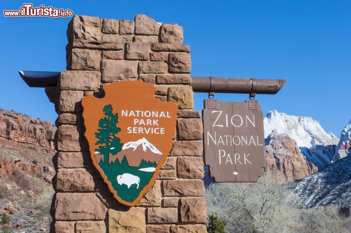 Immagine L'ingresso del Parco Nazionale di Zion, uno dei grandi parchi degli Stati Uniti sud-occidentali, nello stato dello Utah: ogni anno oltre 2 milioni e mezzo di turisti superano questo cartello e si inoltrano tra canyon spettacolari, profonde vallate di grande impatto scenografico e distese di vegetazione lussureggiante. Ben 240 km di sentieri attrezzati attraversano il cuore del parco. Se non vi accontentate di camminare potrete praticare anche l'alpinismo, il torrentismo e l'arrampicata, e da marzo a novembre si possono fare belle gite a cavallo - © Kobby Dagan / Shutterstock.com