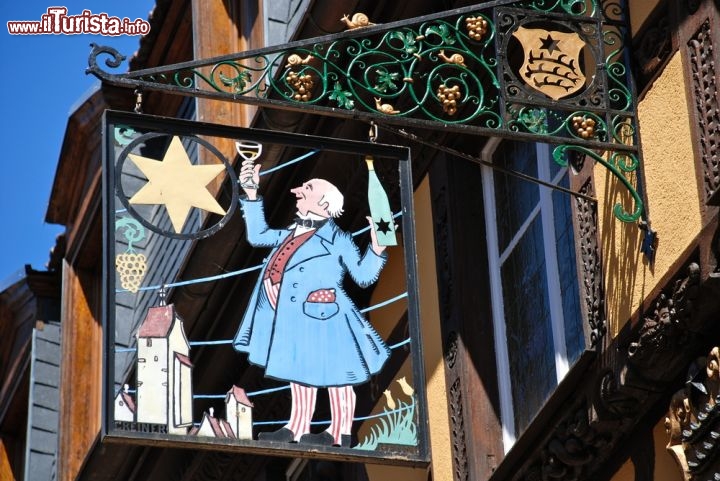 Immagine Insegna pittoresca a Riquewihr, Alsazia - A segnalare a cittadini e turisti le belle botteghe artigianali che impreziosiscono il centro storico di questo borgo francese, considerato uno dei gioielli artistici più preziosi di tutta la Francia, sono le insegne in ferro battuto realizzate con vari soggetti da abili artigiani. In questa immagine la pittoresca insegna all'ingresso di una boutique di vini d'Alsazia  © lucarista / Shutterstock.com