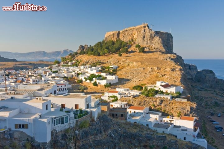 Immagine La rupe e il borgo di Lindos, Grecia - Situata sulla costa orientale dell'isola di Rodi, a circa 50 chilometri dalla città omonima, Lindos si estende su un territorio montuoso e boschivo: il susseguirsi di colline e alture di modesta altezza è intervallato dagli edifici del centro abitato tutti bianco calce. Alle spalle si innalza la rupe che ospita acropoli e castello di Lindo © Birute Vijeikien / Shutterstock.com