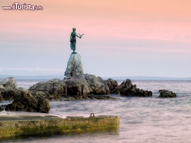 Immagine La ragazza col gabbiano, statua simbolo di Opatija, si staglia contro il rosa del tramonto a due passi dal lungomare cittadino, con lo sguardo verso il mare Adriatico - © Sinisa Botas / Shutterstock.com