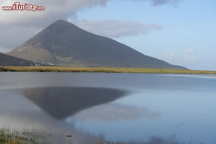 Immagine Foto panoramica di Mount Slievemore, Achill Island - Con i suoi 671 metri di altezza, Mount Slievemore è il secondo picco montuoso (dopo Croaghaun) di quest'isola appartenente al territorio irlandese. In questa immagine l'imponente profilo della montagna si rispecchia nelle acque dell'Oceano Atlantico © Gary Andrews / Shutterstock.com