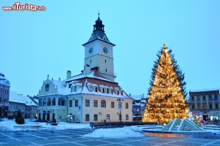 Immagine Municipio Brasov a Natale, Romania - Neve sui tetti del Municipio di Brasov illuminato dalle luci e dalle decorazioni del maestoso albero di Natale che svetta in piazza del Consiglio dove gli abitanti si recano per festaggiare l'arrivo delle tradizionali festività © Cristian Gusa / Shutterstock.com