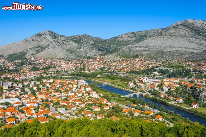 Immagine Fotografia aerea di Trebinje, Bosnia Erzegovina - Attraversata dal fiume Trebisnjica, la città di Trebinje offre un'impagabile vista dall'alto con le sue case dai tetti color mattone che spiccano fra la lussureggiante vegetazione bucolica. Splendida testimonianza architettonica del passato, ad attraversare le sponde del corso d'acqua è l'antico ponte in pietra famoso per la sua struttura che gli consentì di sopravvivere ai bombardamenti della seconda guerra mondiale © Anton_Ivanov / Shutterstock.com