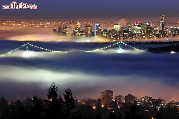 Immagine Un'affascinante veduta di Vancouver (Canada) fotografata dall'alto della Cypress Mountain, la vetta a nord della città che comprende un'importante ski area. Nella foto, immerso nella nebbia, il Lions Gate Bridge illuminato e lo skyline sullo sfondo- © Lijuan Guo / Shutterstock.com