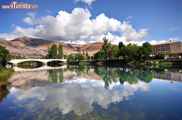 Immagine Foto panoramica di Trebinje, Bosnia Erzegovina - Il ponte in pietra si riflette nelle acque trasparenti del fiume Trebisnjica. Questa costruzione rappresenta uno dei monumenti più importanti dal punto di vista storico e culturale della città e dell'intera Bosnia Erzegovina © Darko Kovacevic / Shutterstock.com