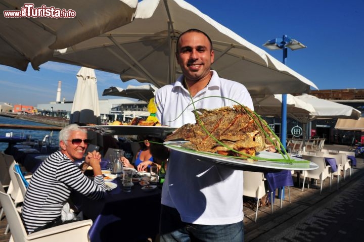 Immagine A Tel Aviv, in Israele, la zona del porto è la più vivace della città. Recentemente restaurata e valorizzata, è piena di negozi e attività commerciali, e sul lungomare si susseguono locali e ristoranti in cui gustare un'ottima cucina a base di pesce fresco  - © ChameleonsEye / Shutterstock.com