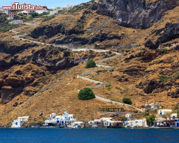 Immagine Thirasia è un'isola vulcanica delle Cicladi (l'arcipelago di Santorini, in Grecia) dal paesaggio brullo e roccioso. Nell'immagine la strada tortuosa che attraversa la macchia e raggiunge il piccolo porto di Korfos, sullo sfondo, lungo la costa orientale dell'isola - © ian woolcock / Shutterstock.com