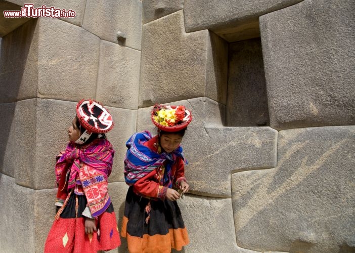 Immagine Ragazze indios con abito tradizionale  - Stoffe colorate e sgargianti caratterizzano gli abiti indossati dalle donne indios che per completare il loro tipico costume indossano anche simpatici cappelli dalle forme più stravaganti. In questa immagine due ragazze di fronte alle rovine peruviane - © Joel Shawn / Shutterstock.com