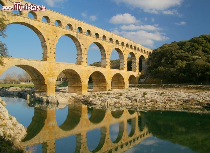 Immagine Riflessi sulle acque del fiume Gardon: è l'inconfondibile silhouette dello storico Pont du Gard, l'antico acquedotto romano che si trova a Vers, in Liguadoca-Rossiglione, nel sud della Francia - © G2019 / Shutterstock.com