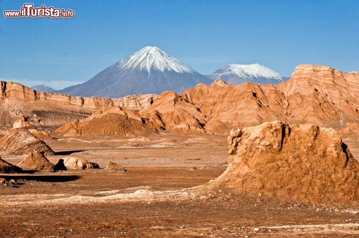 Immagine Vicino a San Pedro Atacama si trova la magica Valle della Luna, una zona tra le montagne caratterizzata dalle rocce di colore arancione, che diventan particolarmente suggestive al tramonto e all'alba. Sullo scondo si vede il profilo del grande vulcano Licancabur, che rimane in direzione del confine con la Bolivia - © Ksenia Ragozina / Shutterstock.com