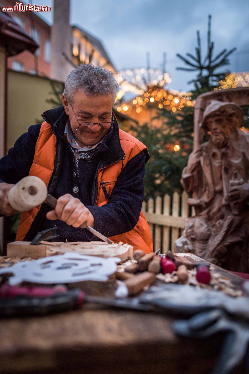 Immagine Un artigiano scolpisce il legno in un mercatino dell'Avvento a Villach, Austria © Hannes Pacheiner