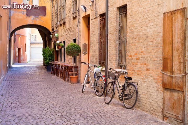 Immagine Centro storico di Ferrara, Emilia Romagna: una delle tipiche strade medievali, con ciottoli, archi e mattoni a vista. La bicicletta è il mezzo ideale per scoprire questa città a misura d'uomo, scivolando tra i monumenti del centro o lungo le mura estensi e i polmoni verdi  - © vvoe / Shutterstock.com