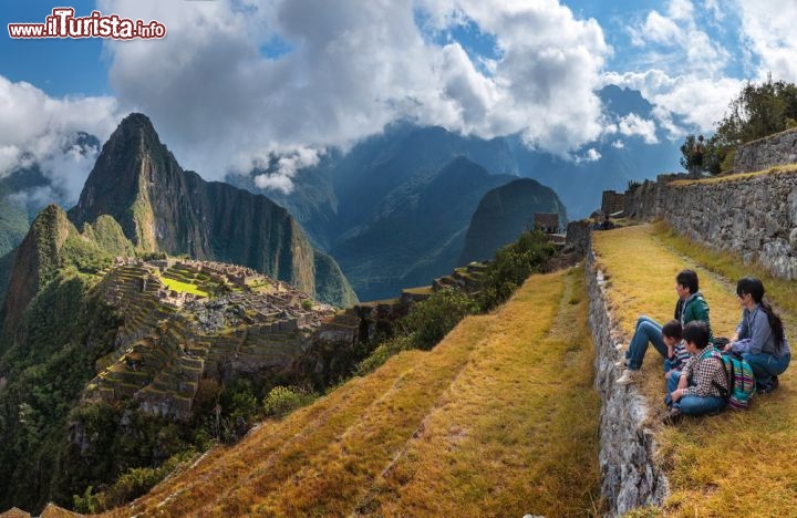 Immagine Vacanza in famiglia a Machu Picchu, Perù  - Il panorama che si gode dai terrazzamenti di fronte al sito archeologico di Machu Picchu lascia senza fiato. In questa immagine, una famiglia ritratta in un momento di relax durante una vacanza in Perù dove l'azzurro del cielo contrasta con le tonalità verdi e gialle della natura che circonda la città inca - © Christian Vinces / Shutterstock.com