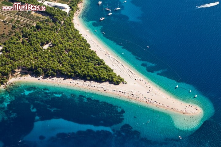 Immagine Zlatni Rat, il corno d'oro, la spiaggia più famosa di Brac, della Dalmazia e forse dell'intero Adriatico. Si trova nella grande isola di Brazza (Brac) in Croazia, la più grande delle isole dalmate. la spiaggia si trova vicino alla città di Bol, grossomodo a metà della costa meridionale di Brac, ed è formata da una fitta pineta trinagolare da cui diparte una barra di sabbie e piccoli ciottoli che, come una lingua, s'allunga per circa 400-500 metri in mare. La spiaggia, al termine della pineta, raggiunge uno spessore di circa 100 metri, ma nonostante le grandi dimensioni tende ad essere sempre affollata, in virtù della sua enorme popolarità - © Simone Simone / Shutterstock.com