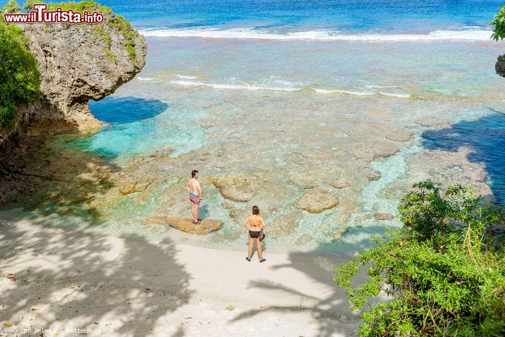 Immagine Alofi, isola di Niue: un uomo e una donna in costume da bagno sulla barriera corallina di fronte alla spiaggia isolata immersa nella vegetazione - © Brian S / Shutterstock.com