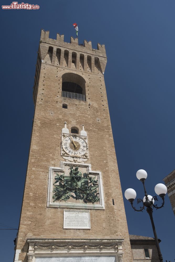 Immagine Antica torre dell'orologio a Recanati, Marche. Alta 36 metri e coronata da una merlatura ghibellina, la Torre del Borgo fu costruita nella seconda metà del XII° secolo. Sulla torre è apposta una targa dedicata ai caduti di Guido Cirilli, un bassorilievo in bronzo che rappresenta la Traslazione della Santa Casa di Loreto, un leone rampante sotto lo stemma cittadino e l'orologio con quadrante del 1562.