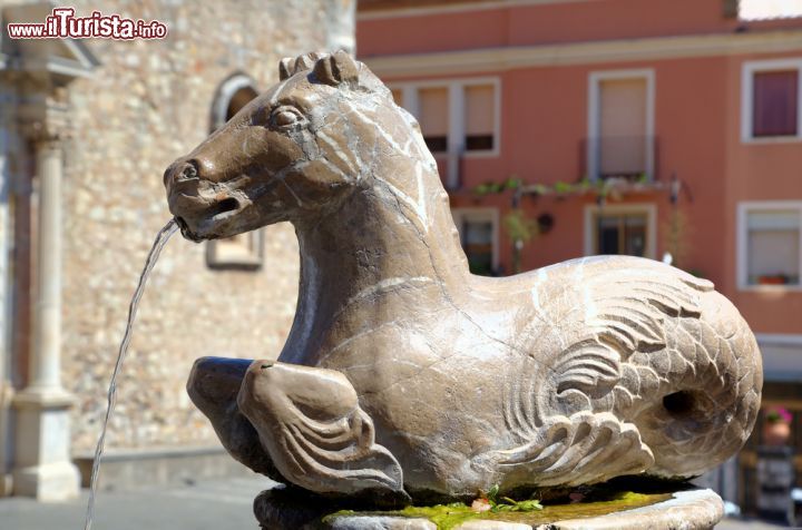 Immagine Antico cavallo di una fontana nella piazza principale di Taormina, Sicilia. Piazza Duomo ospita al suo centro una suggestiva fontana costruita nel 1635 in stile barocco: è formata da due vasche sopra le quali si eleva la statua che raffigura l'emblema della città, il centauro bipede con busto di donna. Ai quattro angoli della fontana, da cui deriva anche il nome "Quattro Fontane", si trovano altrettante colonne su cui vi sono dei cavallucci marini dalla cui bocca, un tempo, sgorgava l'acqua che si riversava nella vasca sottostante.