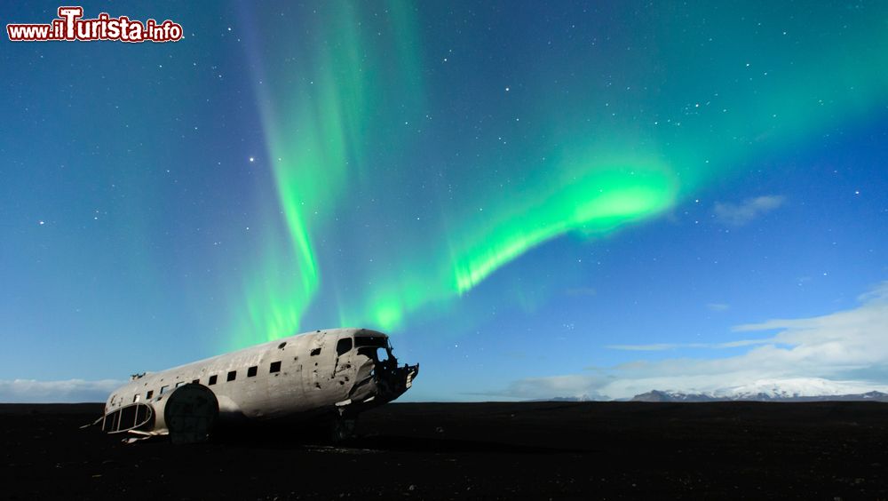 Immagine L'aurora boreale sopra un aereo abbandonato vicino a Vik i Myrdal, Islanda. Questo fenomeno ottico dell'atmosfera terrestre è caratterizzato da bande luminose di un'ampia varietà di colore e forme che cambiano velocemente.