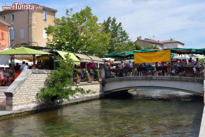 Immagine Bancarelle e tavolini dei caffè affollati lungo le strade e i ponti sui canali della citadina di L'Isle-sur-la-Sorgue, in Provenza - foto © Oleg Znamenskiy / Shutterstock.com
